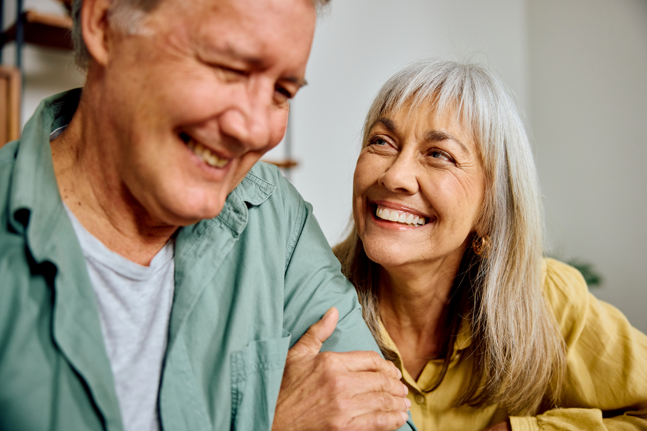 Closeup of a cheerful senior couple sharing laughter and affection while sitting arm in arm at home