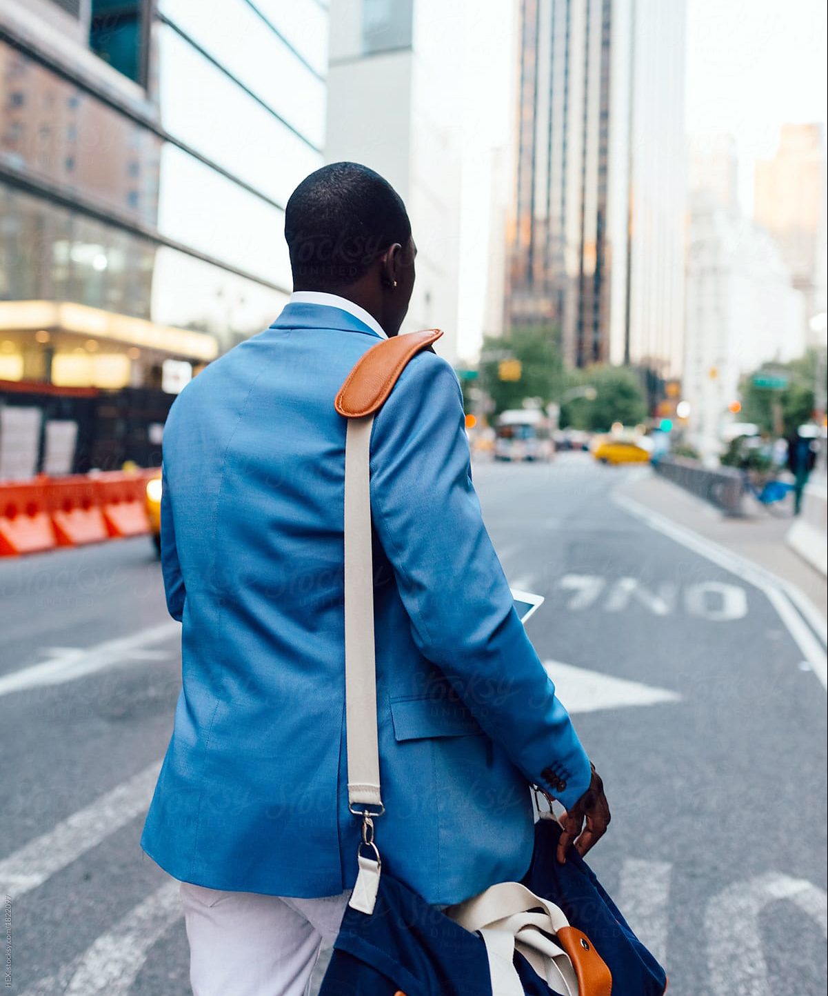 Business man in blue suit jacket holding a cell phone and messenger bag crosses the street