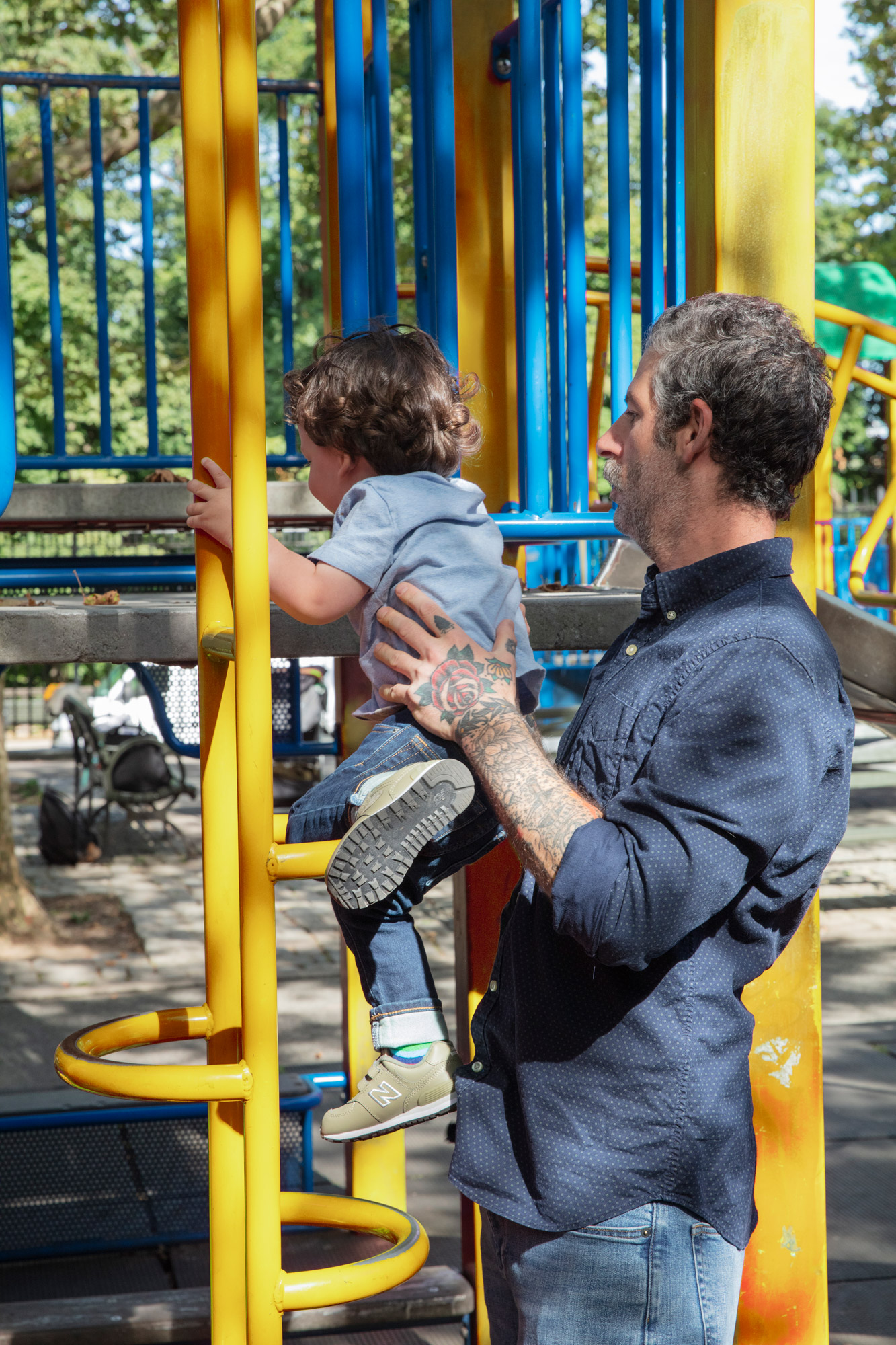 Father helps son up onto a playground equipment at the park
