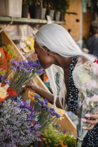 A woman bends down to smell flowers at a storefront
