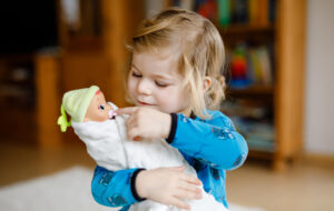 A toddler carefully holds a swaddled baby doll