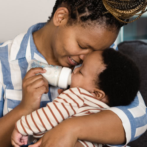 A mother snuggles close with her baby as she feeds them a bottle