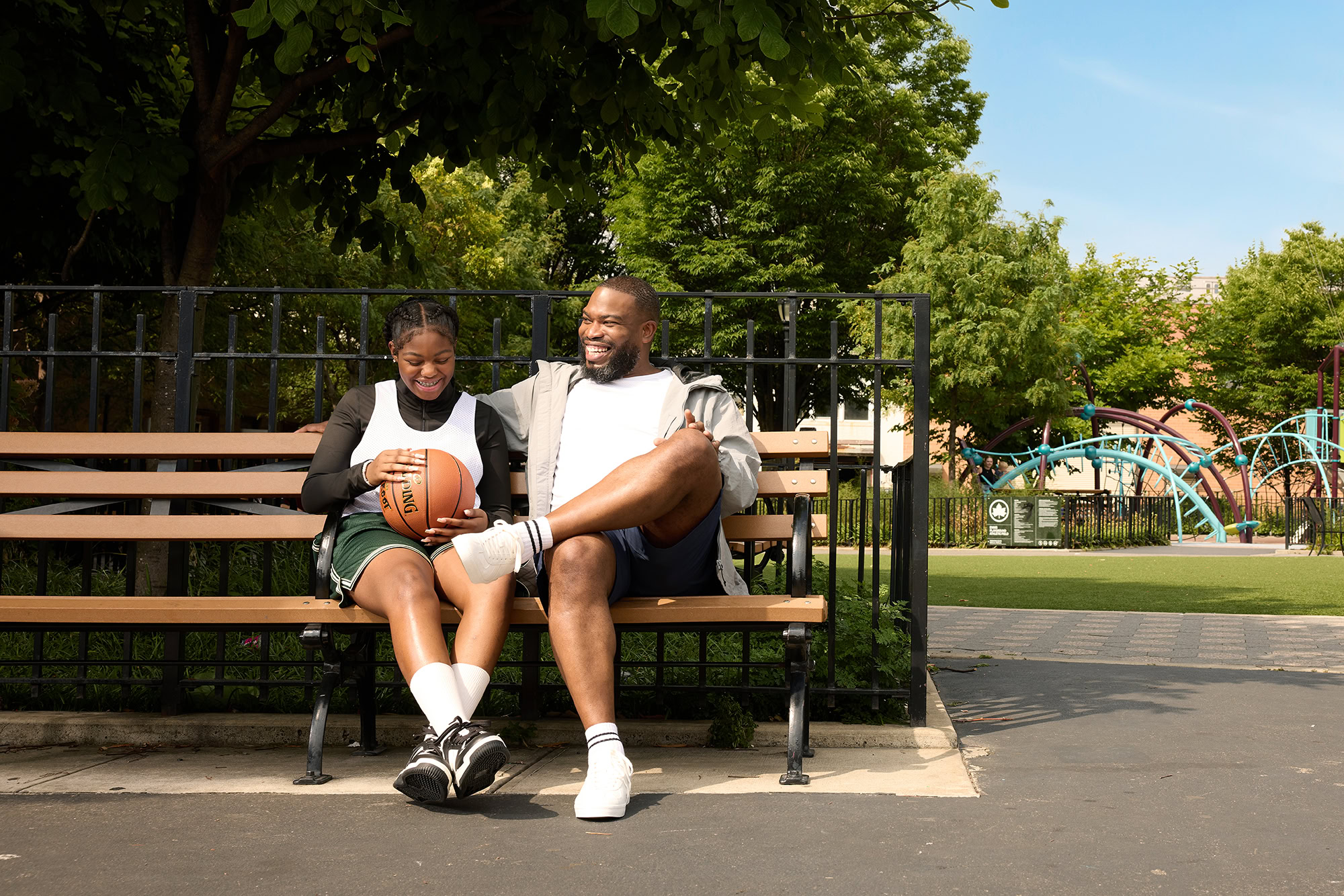 father and daughter sit at new york city park bench holding a basketball