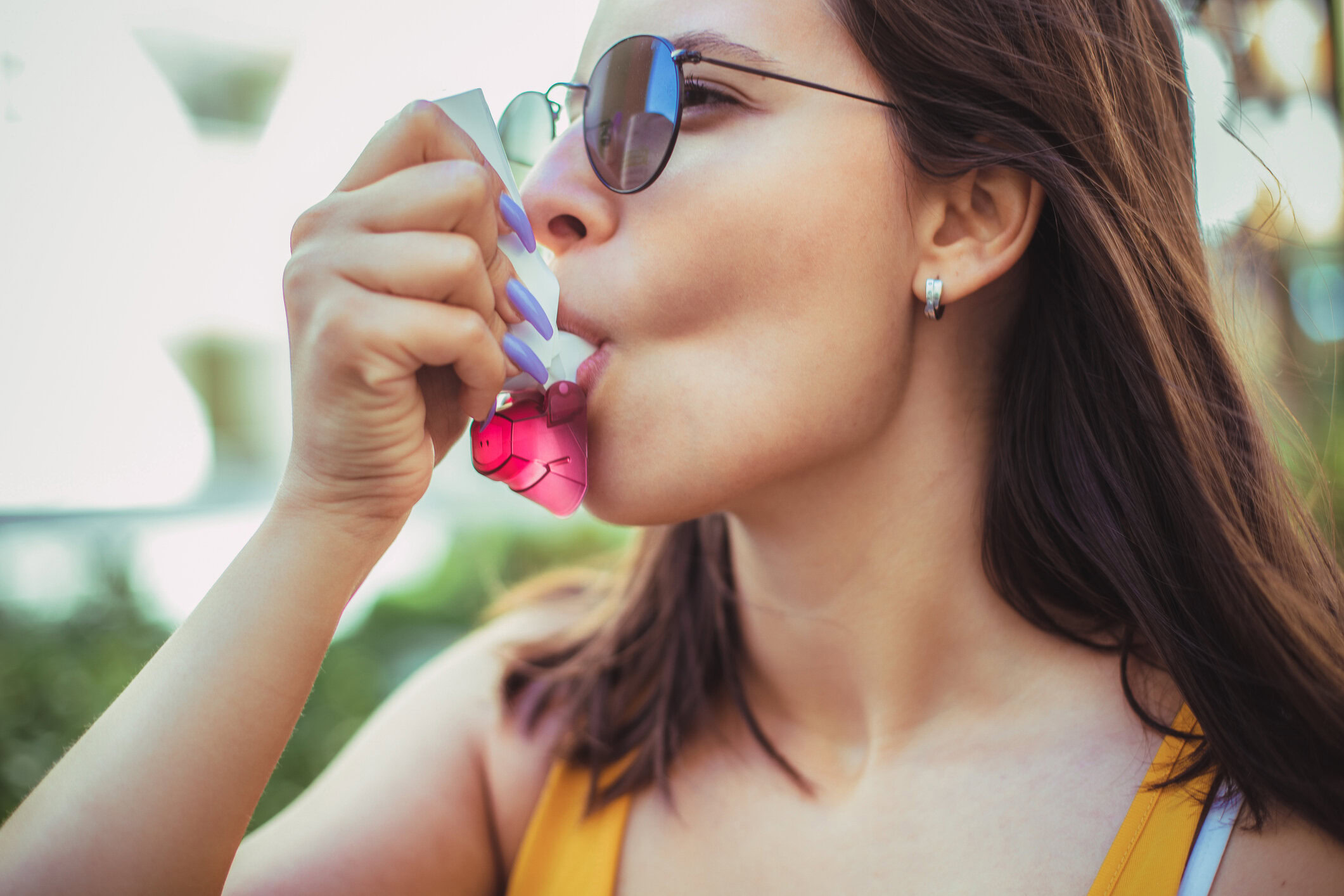 A young woman using an inhaler while sitting outdoors, looking relieved.